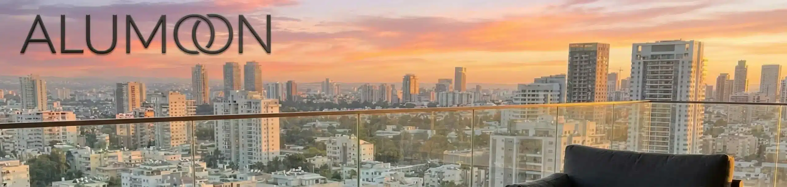 מערכת ישיבה יוקרתית מאלומיניום בצבע אפור פחם מונחת על מרפסת פנטהאוז עם נוף עירוני מרשים של שעת שקיעה, הריהוט מעוצב בקווים נקיים ופתוחים המאפשרים מעבר אוויר